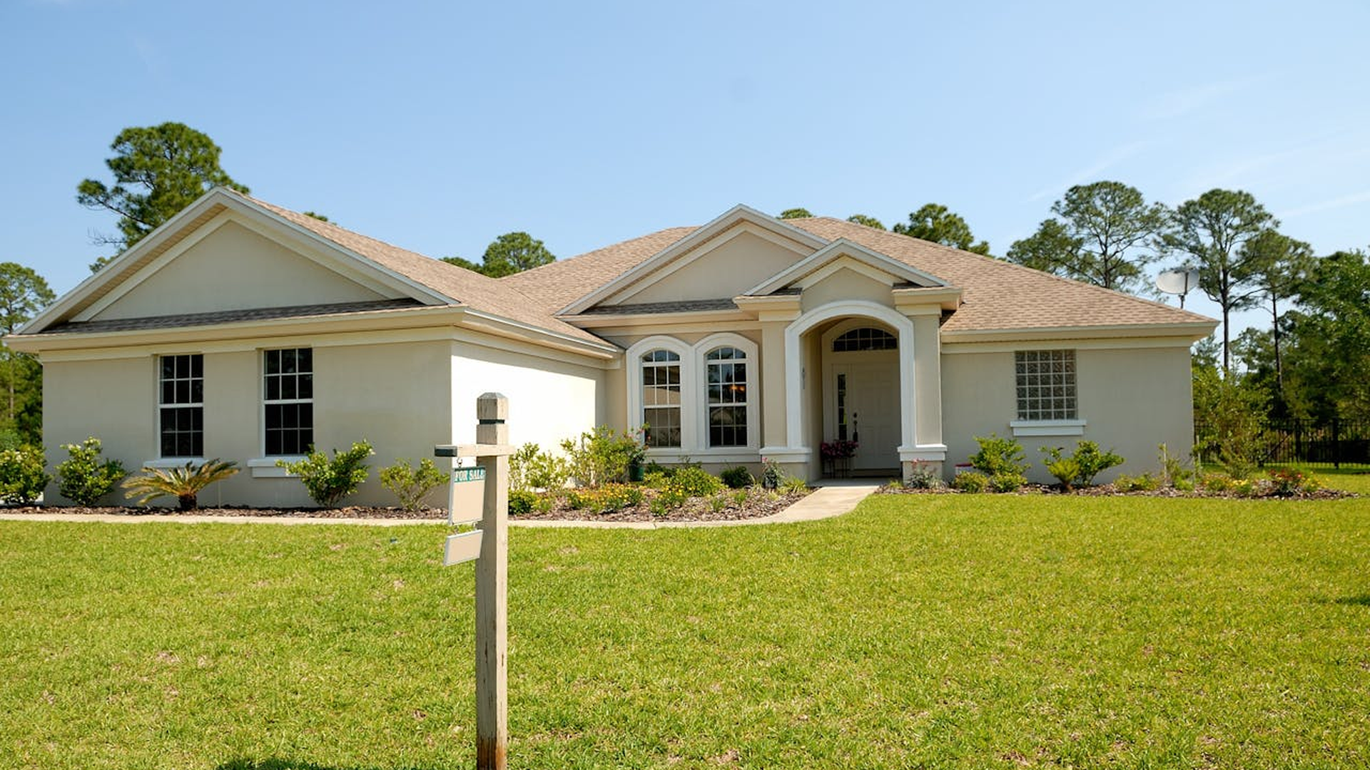 Suburban house with for sale sign on front lawn under blue sky