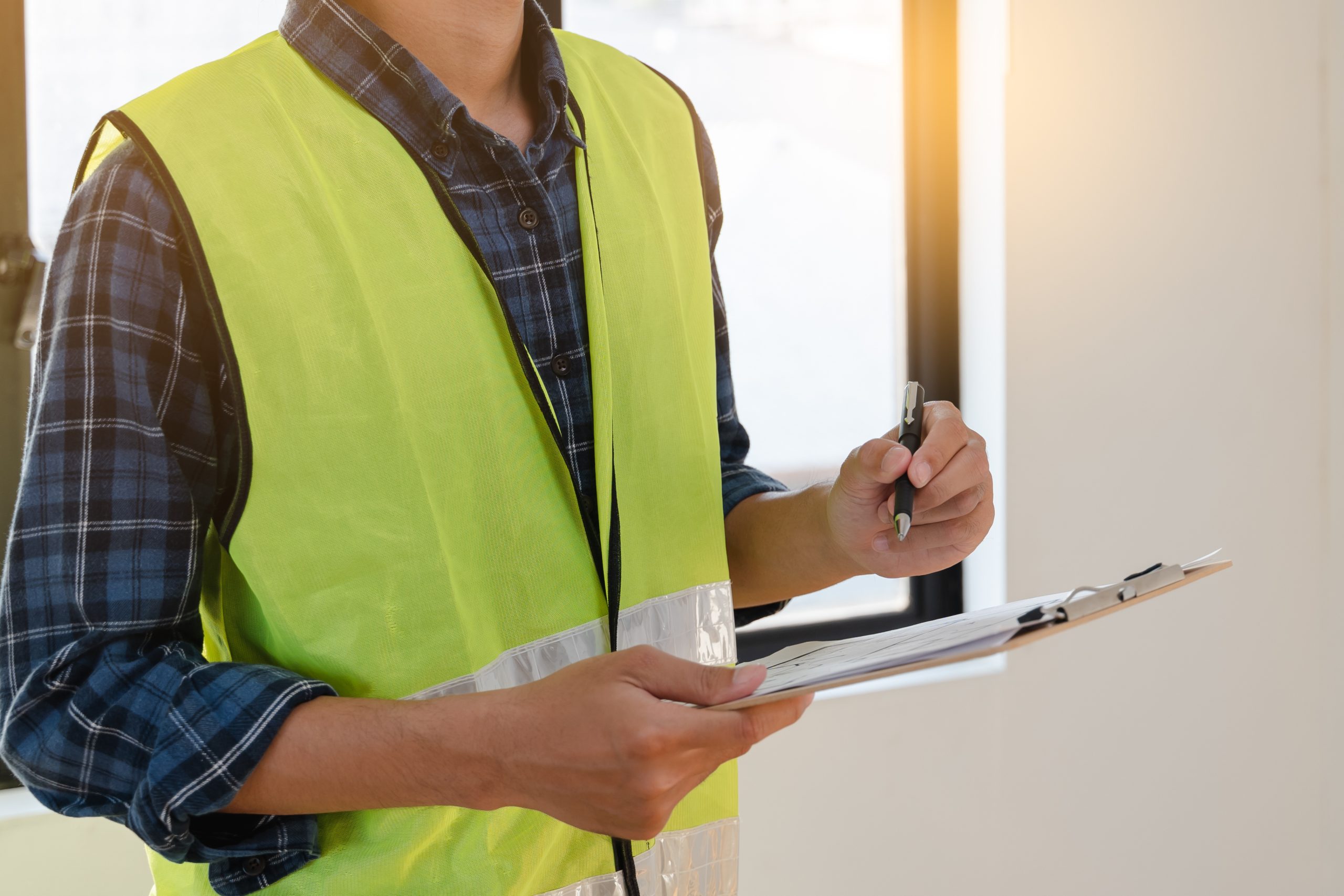 Home inspector in safety vest taking notes on a clipboard during property inspection