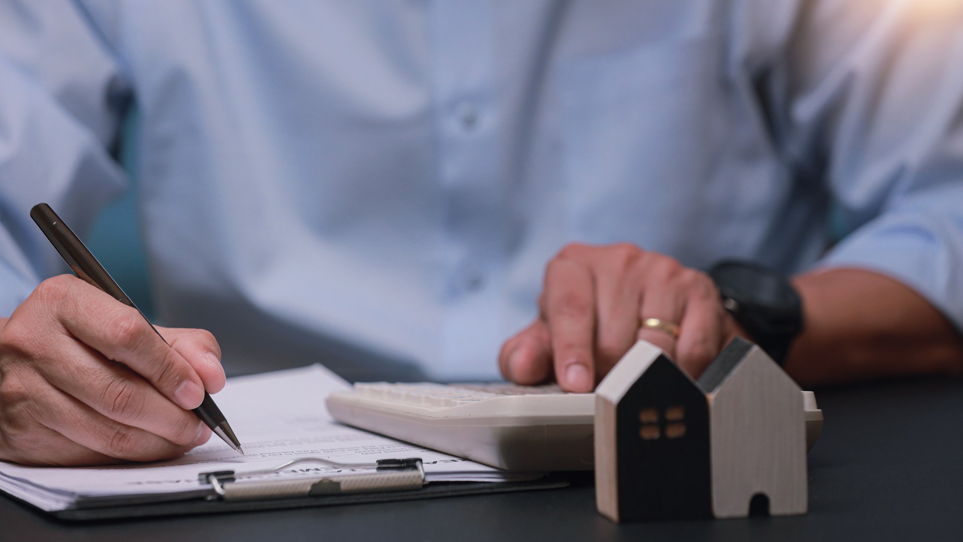 A homebuyer at a desk with loan paperwork, a calculator and a small model house, putting a price on a property.