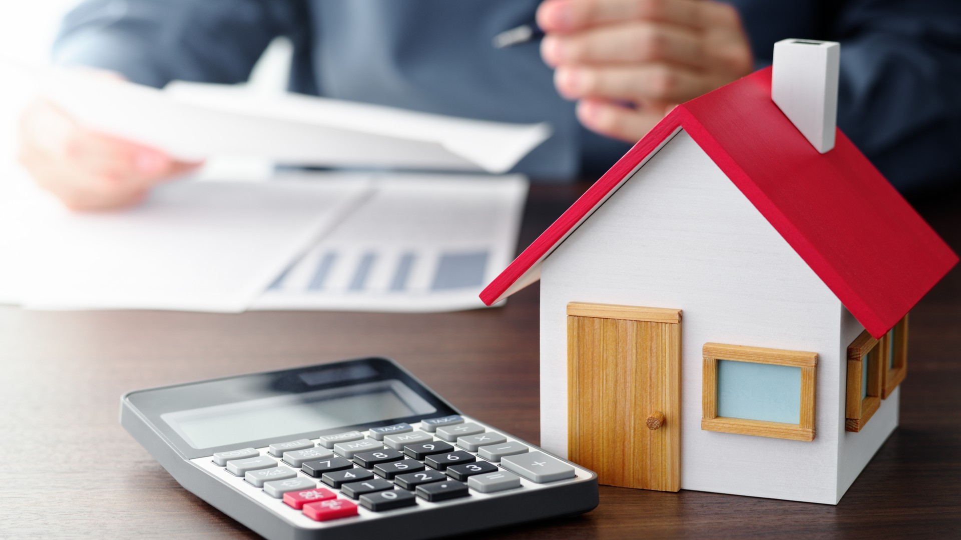 A homebuyer reviewing a real estate contract beside a small wooden house model and a calculator on a wooden table while weighing the cost of a Bucks County home inspection.