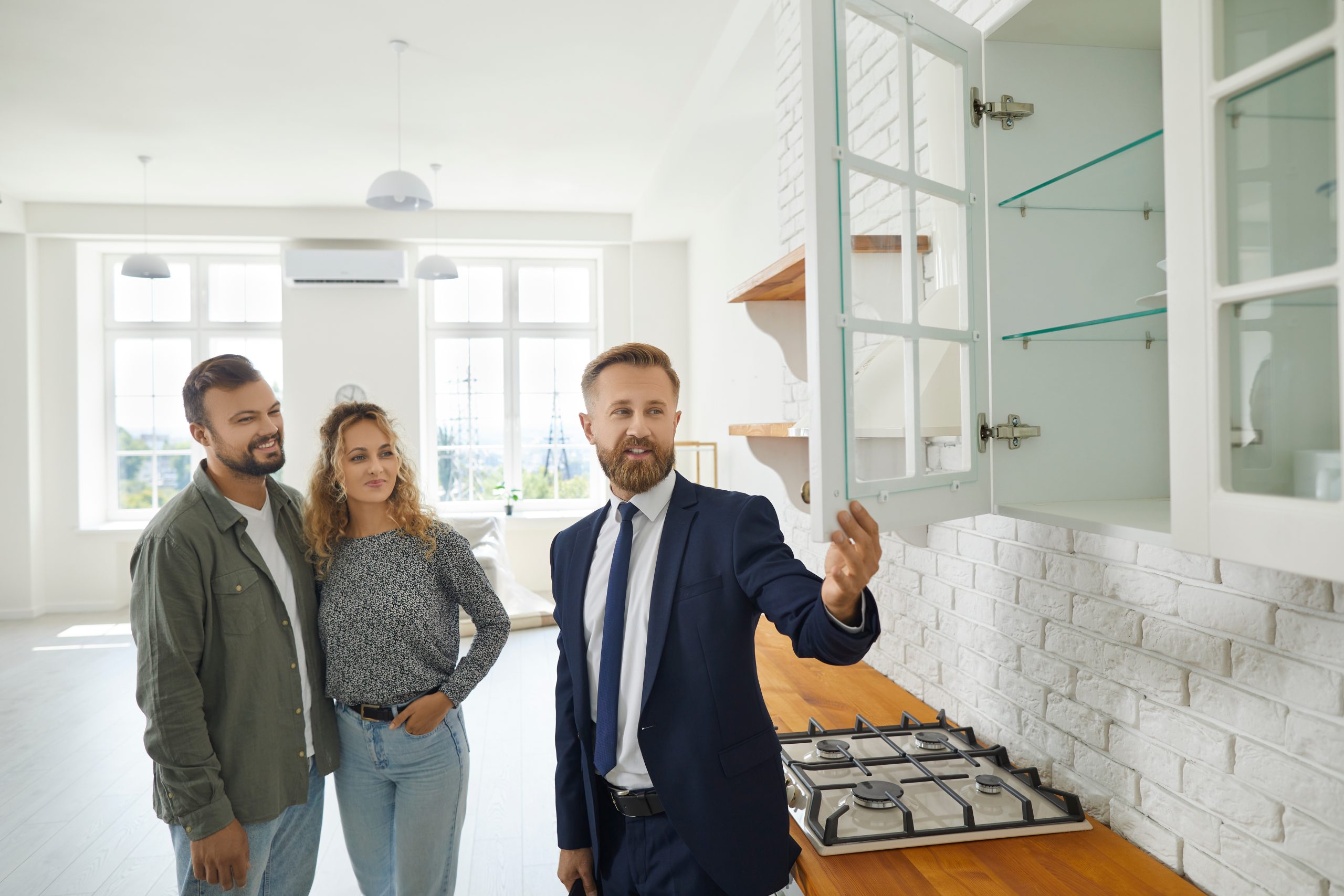 A young first-time-buyer couple walks through a sunlit suburban home with their real-estate agent, talking through what to look for at the inspection walkthrough.