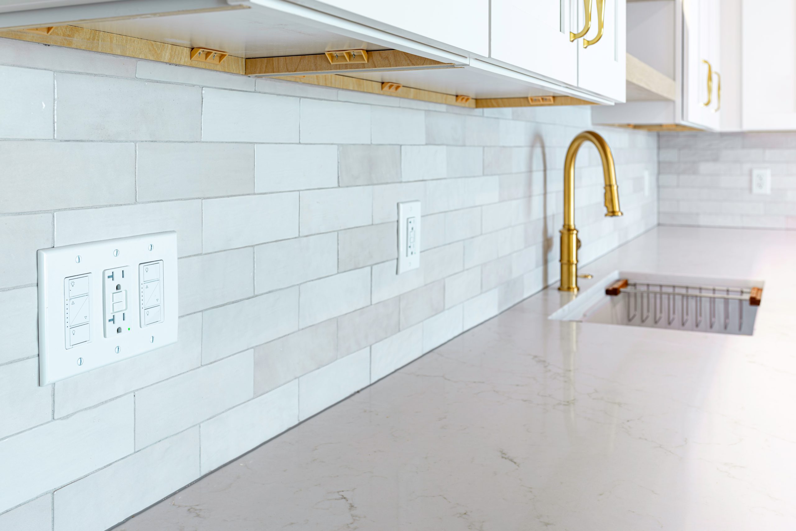 Close-up view of a three-gang electrical wall plate with integrated light switches and a GFCI outlet installed on a white tile kitchen backsplash near ... See More