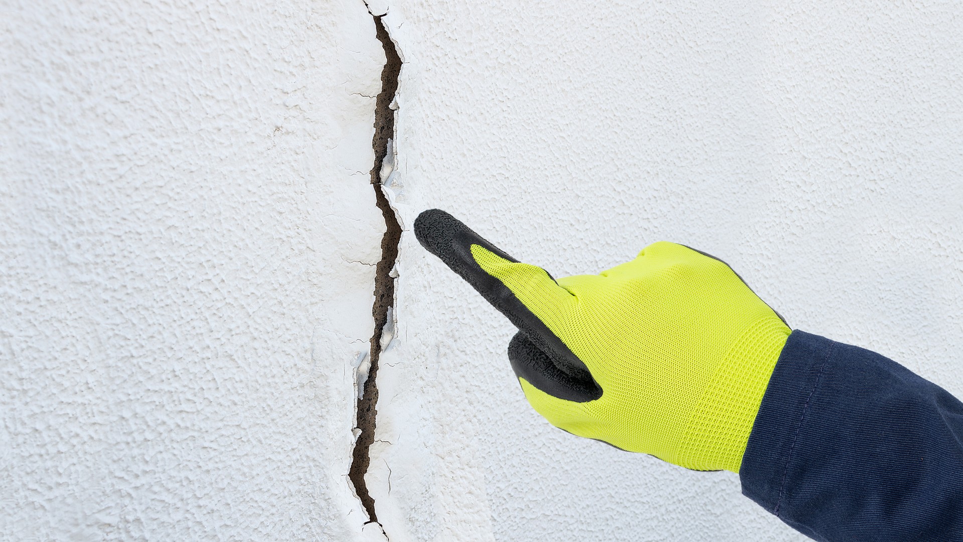 A licensed home inspector using a handheld moisture meter against the exterior stucco wall of a suburban Pennsylvania home near a first-floor window, checking for hidden water damage behind the stucco surface.