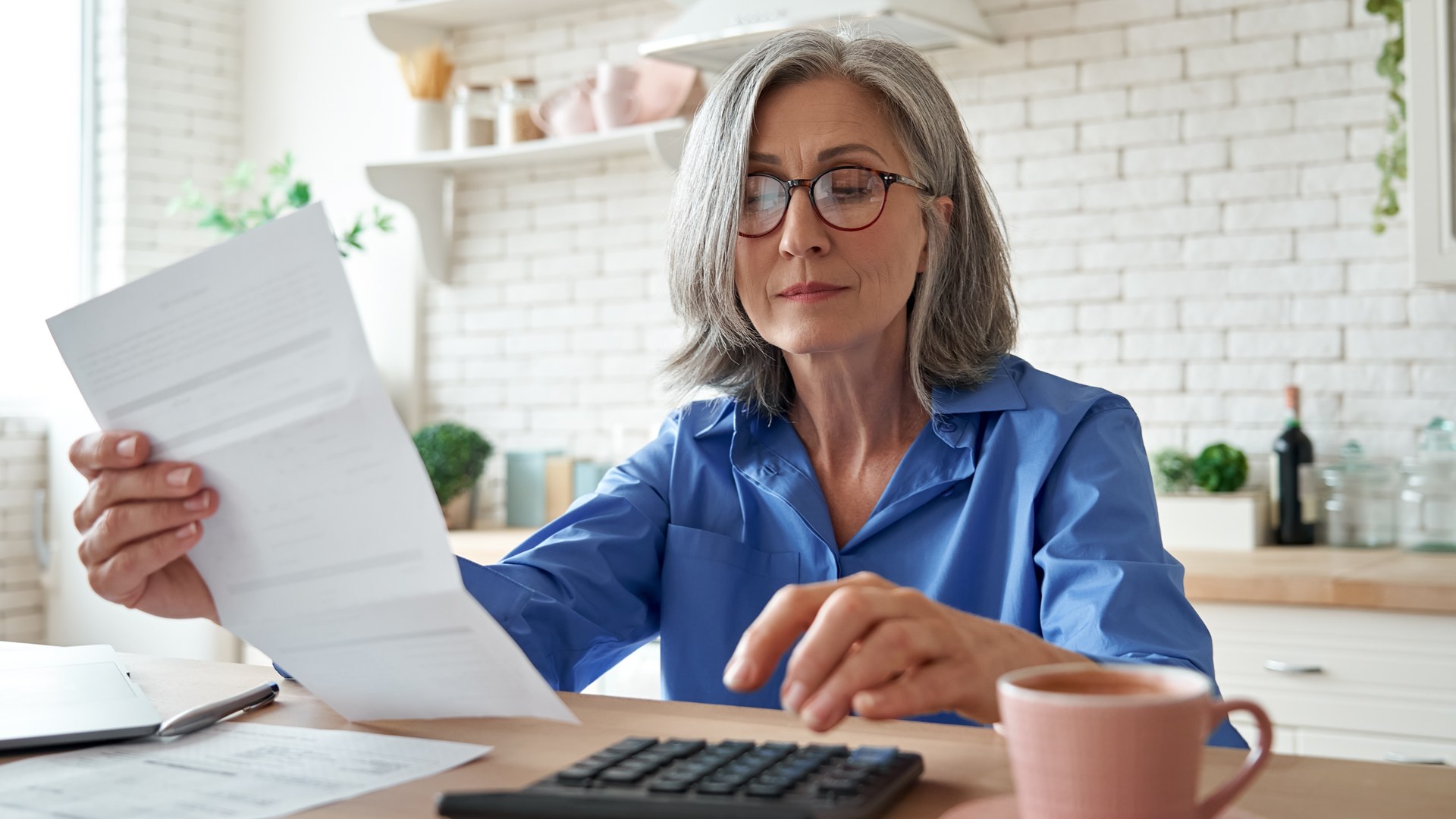 A home buyer at a kitchen table reading a multi-page inspection report with one hand on a calculator, planning which repairs to budget for after closing.