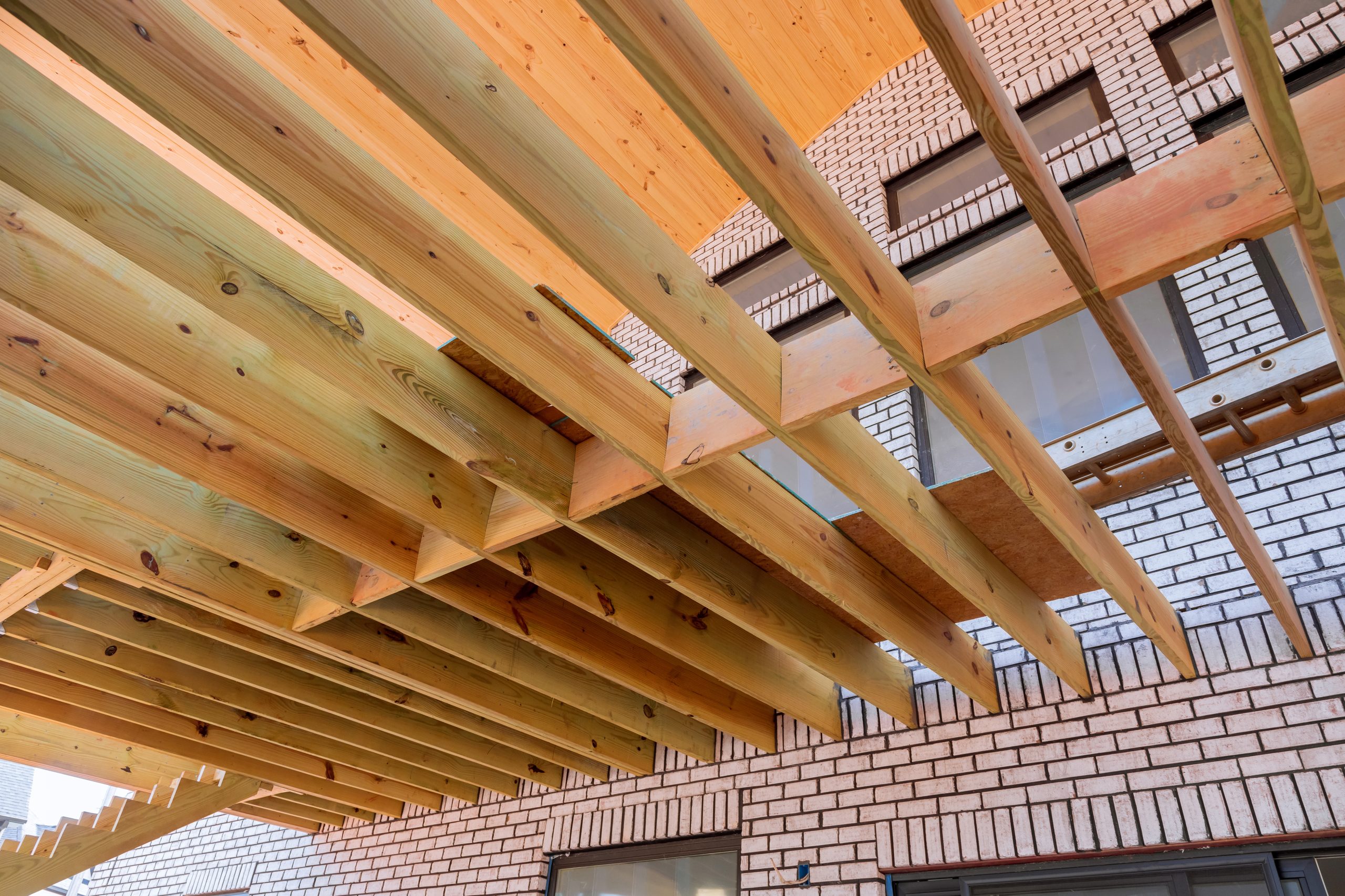 View from below of a wood deck frame, with joists and beams running toward the brick wall of a house