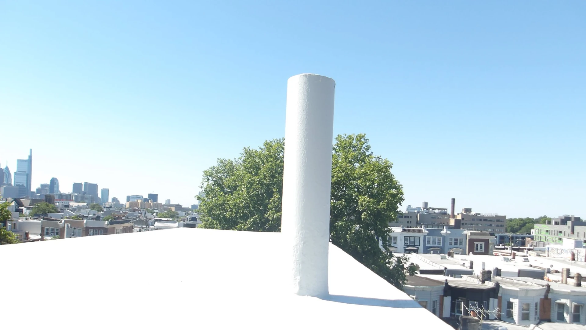 A white-coated flat roof with a vent stack overlooks Philadelphia row homes and the Center City skyline.
