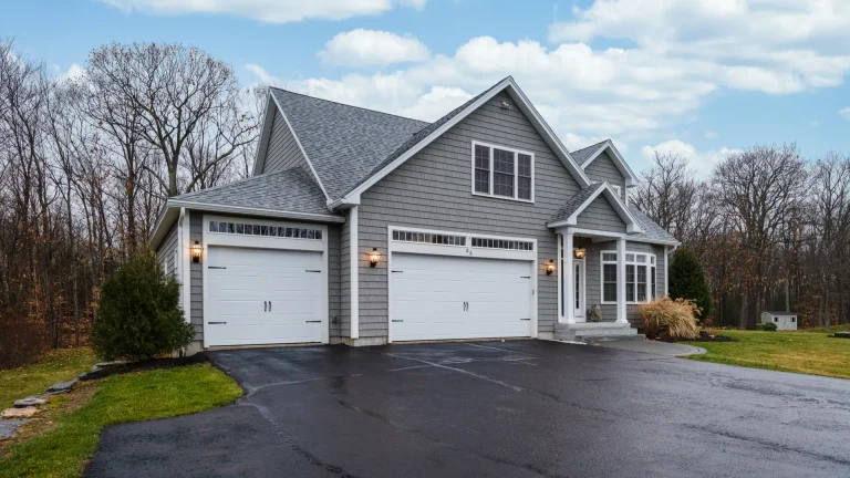Gray shingle-sided house with two white garage doors and a paved driveway
