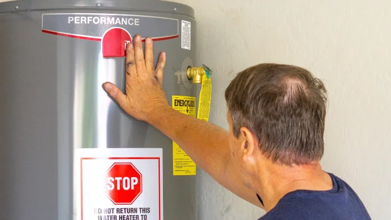 Man resting a hand on a gray water heater near its yellow EnergyGuide label