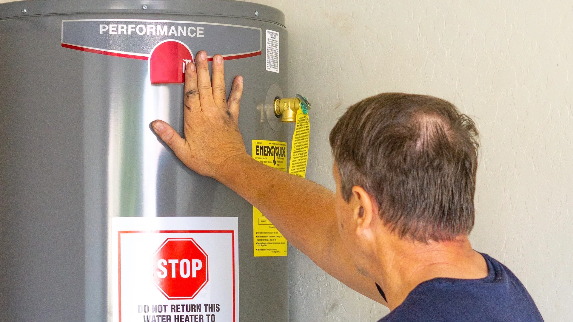 A man examines the control area and yellow EnergyGuide tag on a residential gas water heater