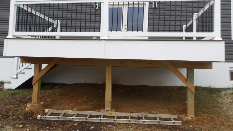 Elevated deck with white railings, wooden support posts with diagonal bracing standing on bare soil, and a ladder lying on the ground beneath it